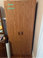 Closed wardrobe showing woodgrain finish and two black handles on the doors.