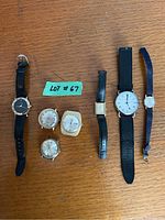 Image of six watches and watch parts arranged on a wooden surface with a green label 'Lot #67'.