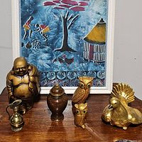 Photo of all items showing Buddha statue, urn, brass pitcher vase, two owl statues, and ceramic dove figurine in front of framed artwork, placed on wooden surface.
