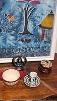 Wide view of all 4 lot items together with artwork background, showing the Sevillaby Bobby Flay lugged bowl, modern sculpture, demitasse cup & saucer, and wood decorative item