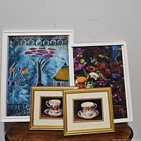 Set of three framed artworks: bright tribal scene, dark floral painting, and two gold framed tea cups paintings