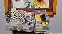 Three clear plastic bins stacked with various supplies including electrical cords, painting tools, and hardware items.