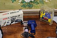 Coleman Inflate-All portable air compressor, power cord, and clear plastic case containing inflation kit nozzles on wooden surface