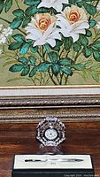 Waterford crystal clock and Cross chrome pen side by side on a wooden surface with a floral painting background