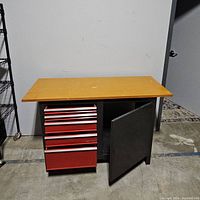 Front view of the workbench with wood top, showing five red drawers and an open side cabinet door.