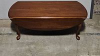 Front view of the coffee table highlighting Queen Anne style cabriole legs and drop leaf sides in folded position.
