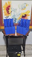 Photo of six blue plastic file folder dividers arranged on a wooden table with a sunflower painting behind and a black portable file box on the floor beneath the table.