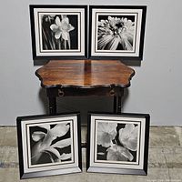Four black and white floral prints arranged around and on a wooden side table showing overall lot