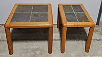 Two teak wood side tables with slate tile inset tops, one rectangular and one square, shown side by side on concrete floor.