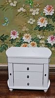 Front view of closed white jewelry box showing three drawers and side compartments closed.
