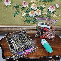Photo showing metal divider tray with assorted flatware and flatware with child utensils, large zip-lock bag of cookie cutters, and teal Kitchen Mama can opener.