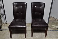 Front view of set of two dark brown vinyl tufted dining chairs with cherry legs.