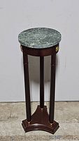 Full view of the round green marble top plant stand, showing its cherry wood base and three vertical legs connected to a triangular base.
