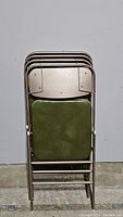 Four vintage metal folding chairs stacked together showing seats and metal frames.
