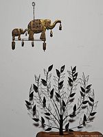 Photo of the elephant wind chime and the large metal wall tree hanging side by side on a white wall.