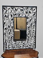 Front view showing the rectangular mirror centered in an ornate black wire floral frame with leaves and flowers.