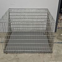 Front view of metal dog crate showing double door locks and removable metal tray base on concrete floor.