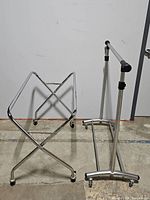 Laundry rack with X-shaped chrome metal frame and caster wheels, standing on concrete floor.