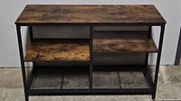 Front view of rustic brown console table showing main top surface and two wooden shelves underneath within black metal frame.