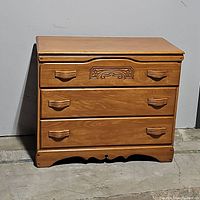 Full front view of the chest of drawers showing three drawers and wooden handles.
