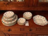 Overall view of stacks of large dinner plates, salad plates, soup bowls, saucers and the handled square cake plate on wooden buffet
