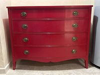 Full front view of red painted four-drawer dresser against wall