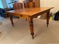 Angled front view showing tabletop, one drawer front and turned cherry leg with brass caster