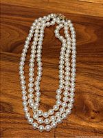 Full view of triple-strand natural pearl necklace on wooden surface