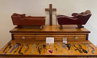 Wooden cabinet top with two doll cradles (not part of lot), central wooden crucifix, various rosaries and religious medals laid out.