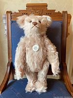 Front view of the rose-beige Steiff teddy bear seated on chair, showing embroidered nose and chest medallion tag