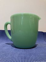 Front view of green Jadite Fire King pitcher showing rounded shape, handle, and spout