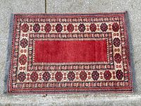 Full view of rug laid flat showing red central field and patterned border