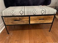 Front view of bench showing upholstered seat with geometric patterns and two wooden drawers in metal frame.