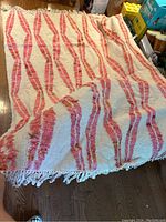 Full view of the cream colored rug with pink and orange geometric patterns spread out showing the fringed edges.