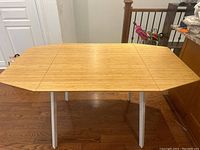 Photo of Ikea dining table in fully extended position with both drop leaves up, showing rectangular wood finish top and white legs.