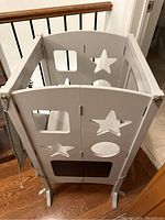 Front view of the white wooden kitchen helper with star, square, and oval cutout shapes on the sides, standing on wooden floor.