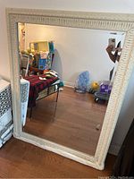 Full view of the off white hanging mirror leaning against a wall showing the mirror and part of the frame.