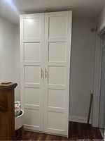 Photo showing the full view of a tall white wardrobe cabinet with two doors and flat panel design.