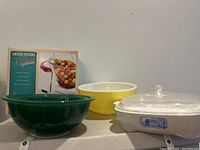 Photo showing the three green Pyrex nesting bowls, yellow bowl, clear lid and white Corning baking dish with blue design, along with Anchor Hocking box.