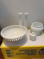 Entire set of five milk glass pieces on a cardboard box, showing two tall vases, one lattice bowl, one hobnail covered jar, and one ornate pot.