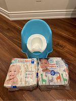 Photo showing blue Babybjorn potty chair with white removable inner potty along with two unopened bags of Honest size 6 diapers.