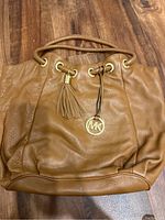 Front view of brown leather Michael Kors purse with tassel and gold-tone hardware on wooden surface.