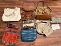 Top-down view of 10 assorted purses and bags arranged on wood floor, showing variety of colors, materials, and styles.