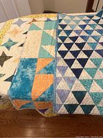 Three quilts stacked and showing variety of patchwork designs including star patterns and teal-orange blocks.