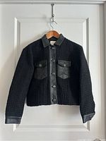 Full front view of black textured jacket with leather collar, button front, and chest pockets.