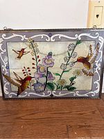 Frontal view showing the entire stained glass piece with hummingbirds and flowers, including the decorative grey and white border.