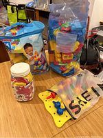 Photo showing Mega Bloks sets in a large plastic bag, foam alphabet letters in a jar, and a yellow pegboard partially inside a mesh bag.