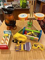 Overall view of lot including Mr. Potato Head figure, Hape drum, wooden toolbox with tools, gloves and goggles placed on table.