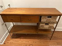 Full front view of West Elm wooden and metal console table with two drawers and two woven baskets on shelf