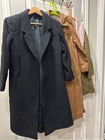 Dark gray tailored wool blend coat hanging on a door with visible lapels and smooth fabric texture